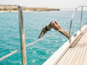 Person diving from luxury charter boat deck into crystal-clear turquoise Caribbean waters off Aruba's golden coastline