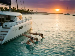Luxury white catamaran anchored in turquoise Caribbean waters near Aruba with passengers swimming at golden sunset