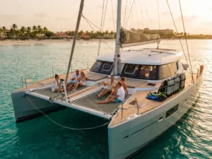 Luxury catamaran sailing turquoise Caribbean waters at sunset with passengers and snorkel gear, Aruba coastline visible