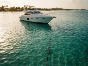 Luxury white yacht anchored in crystal-clear turquoise Caribbean waters with visible anchor chain and sandy bottom below